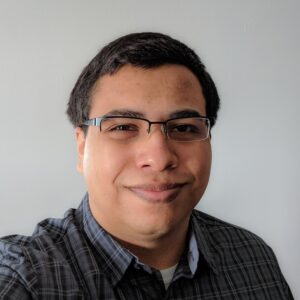 A picture of Jordan Aguilar smiling while wearing glasses, and a collared shirt.